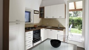 A modern kitchen with white cabinets, a black stove, and a glass table. - Dolce Mare 2 - Sea Front Apartment - Large Terrace - Wifi and Private Parking (Modica)