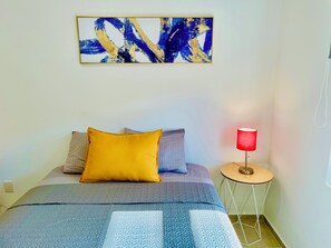 Une chambre à coucher avec un lit, des oreillers, une table de chevet avec une lampe et une œuvre d’art murale.