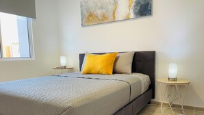 A bedroom with a bed, two bedside lamps, a window, and a wall-mounted abstract painting. - Mayakoba Cozy 2-bedroom Apartment With Amenities (Playa del Carmen)