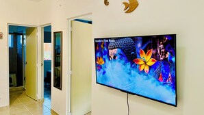 A hallway with a television displaying Buddha Flute Music, a Buddha statue, and three wooden crescent shapes on the wall. - Mayakoba Cozy 2-bedroom Apartment With Amenities (Playa del Carmen)