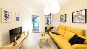 Ein modernes Wohnzimmer mit einem gelben Sofa, einem Flachbildfernseher und Kunstwerken an den Wänden.
