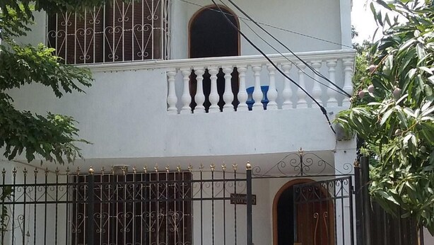 A white building with a gated entrance, a balcony with balustrades, and a window with decorative iron bars. - Room in House - Taminaka Hostel in Santa Marta - Private Room (Santa Marta)