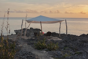 A beach with a canopy and two wooden chairs facing the sea.