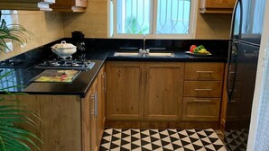 A kitchen with wooden cabinets, a black countertop, a sink, a stove, and a refrigerator. - Cozy And Comfort 2br-2bt Apartment In Centralsosua (Sosúa)