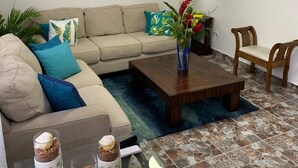 A living room with a beige sofa, a coffee table, a TV, a ceiling fan, and a painting on the wall. - Cozy And Comfort 2br-2bt Apartment In Centralsosua (Sosúa)