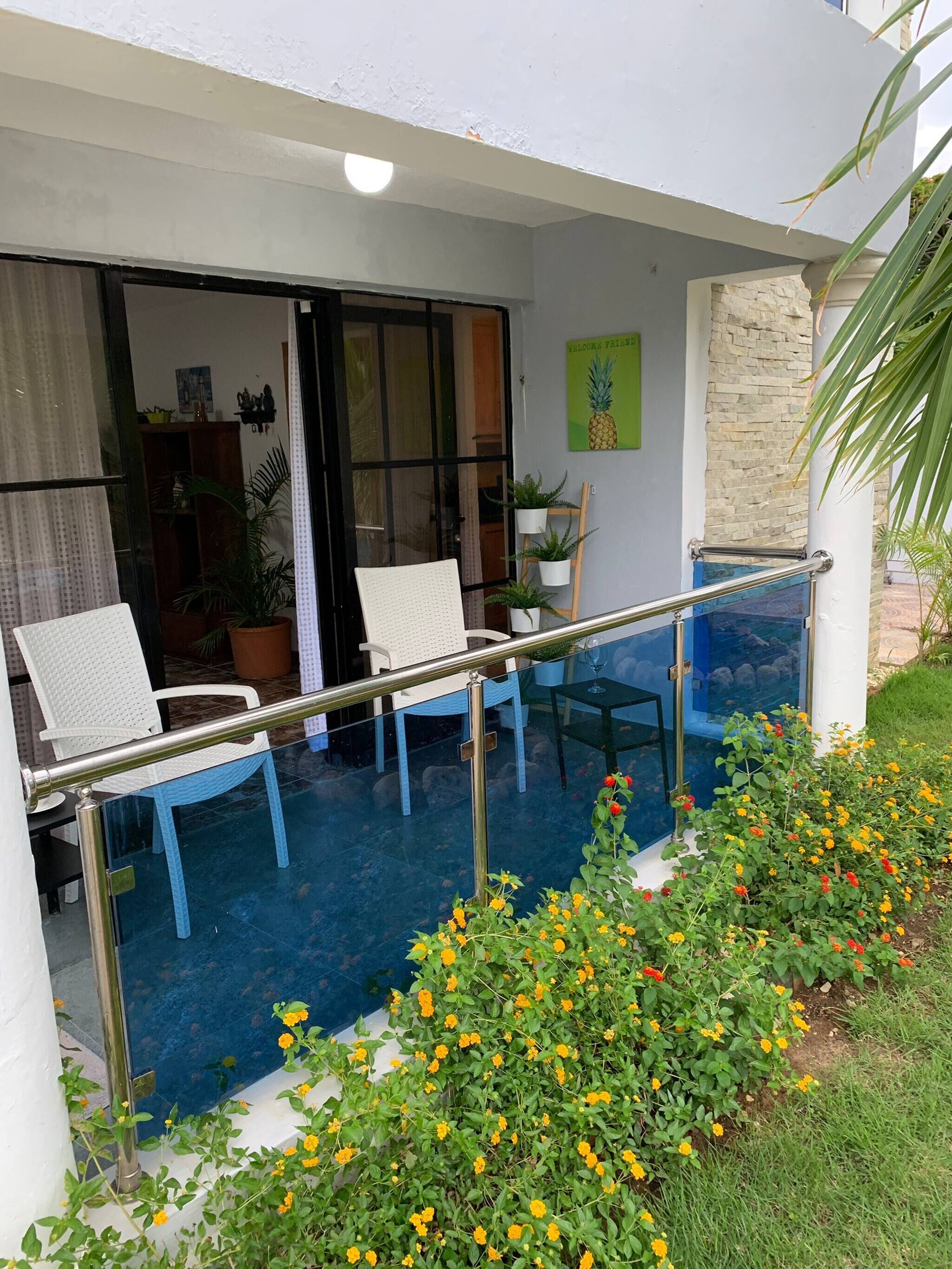 A balcony with two white chairs, a glass table, and a metal railing.