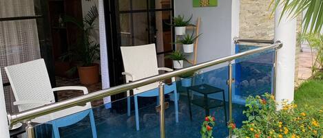A balcony with two white chairs, a glass table, and a metal railing.