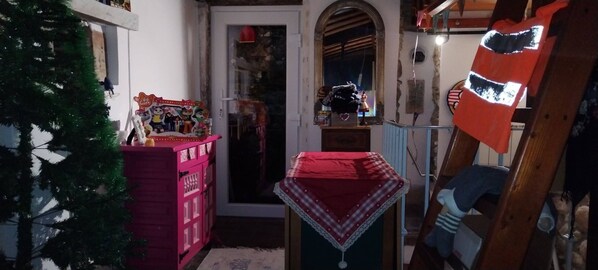 Un pasillo estrecho con una puerta de madera, una mesa pequeña con un mantel rojo y un árbol de Navidad.