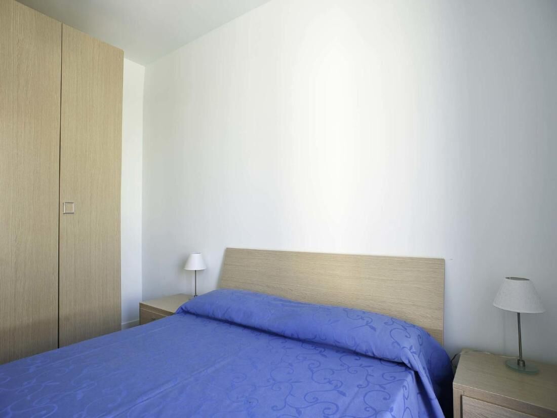 A bedroom with a bed, two bedside tables, a nightstand, and a wardrobe.