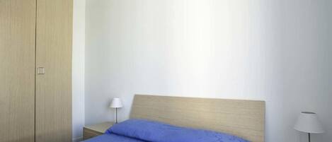 A bedroom with a bed, two bedside tables, a nightstand, and a wardrobe.