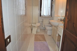 A narrow bathroom with a toilet, bidet, and sink.