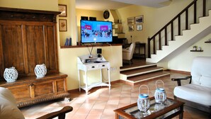 Uma sala de estar com televisão, móveis de madeira, uma escada e uma cadeira branca.