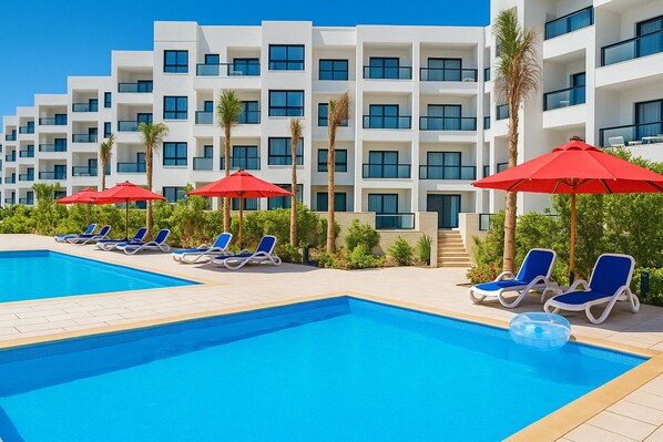 Un hotel moderno con piscina, tumbonas y sombrillas rojas.
