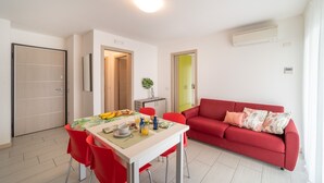 A modern living room with a red sofa, a dining table with breakfast items, and a bright ceiling light. - Elegant Residenza Monica 2 Two Bedroom C6 Sleeps 6 (Lignano Sabbiadoro)