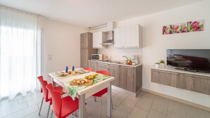 A modern kitchen with white cabinets, a microwave, and a coffee maker. There is a dining table with red chairs and a TV on a stand. - Elegant Residenza Monica 2 Two Bedroom C6 Sleeps 6 (Lignano Sabbiadoro)