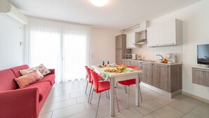 A modern apartment with a dining area, kitchenette, and a living room with a red sofa. - Elegant Residenza Monica 2 Two Bedroom C6 Sleeps 6 (Lignano Sabbiadoro)