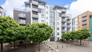 Un moderno edificio de apartamentos con varios balcones y un patio con árboles y pilares.