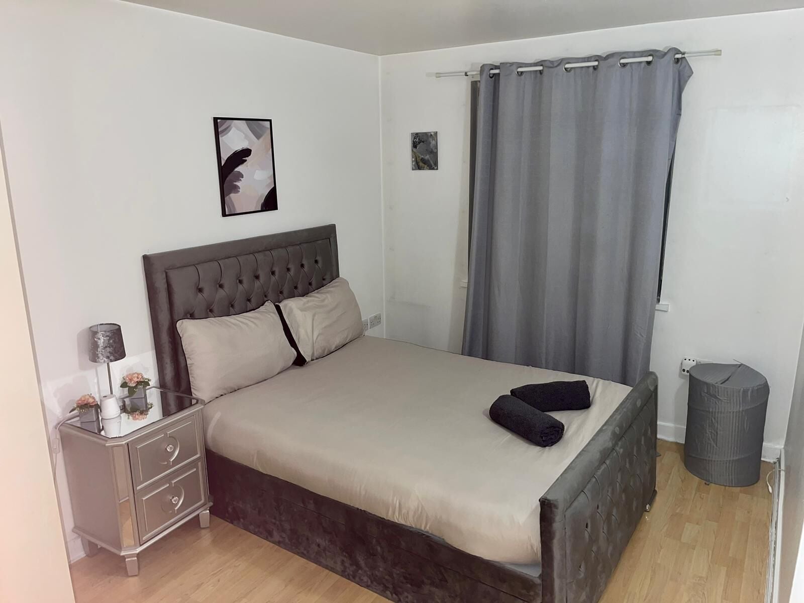 A bedroom with a bed, a bedside table, a lamp, a picture on the wall, and a curtain.