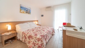 A hotel room with a bed, bedside tables, a desk, a chair, and a window with curtains. - Elegant Residenza Monica Two Bedroom C6 Sleeps 6 (Lignano Sabbiadoro)