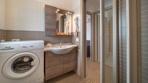 A compact bathroom with a washing machine, a sink, and a glass shower enclosure. - Elegant Residenza Monica Two Bedroom C6 Sleeps 6 (Lignano Sabbiadoro)