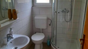 Un baño con lavamanos, inodoro y cabina de ducha con mampara de vidrio.