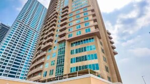 A tall hotel with multiple floors and a parking lot in front. - Homesgetaway - JLT Lake Views 1BR (Dubai)