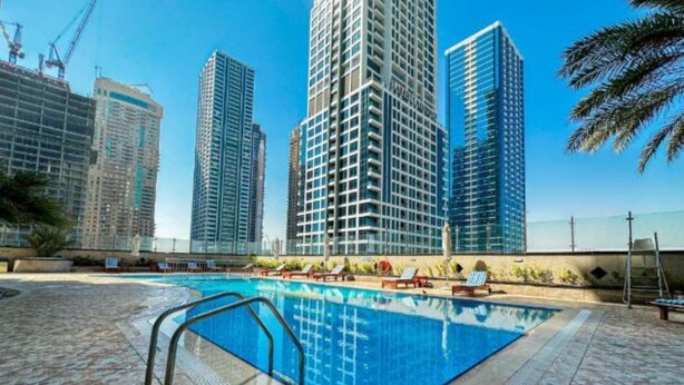 A swimming pool with a tiled deck, surrounded by high-rise buildings and palm trees. - Homesgetaway - JLT Lake Views 1BR (Dubai)