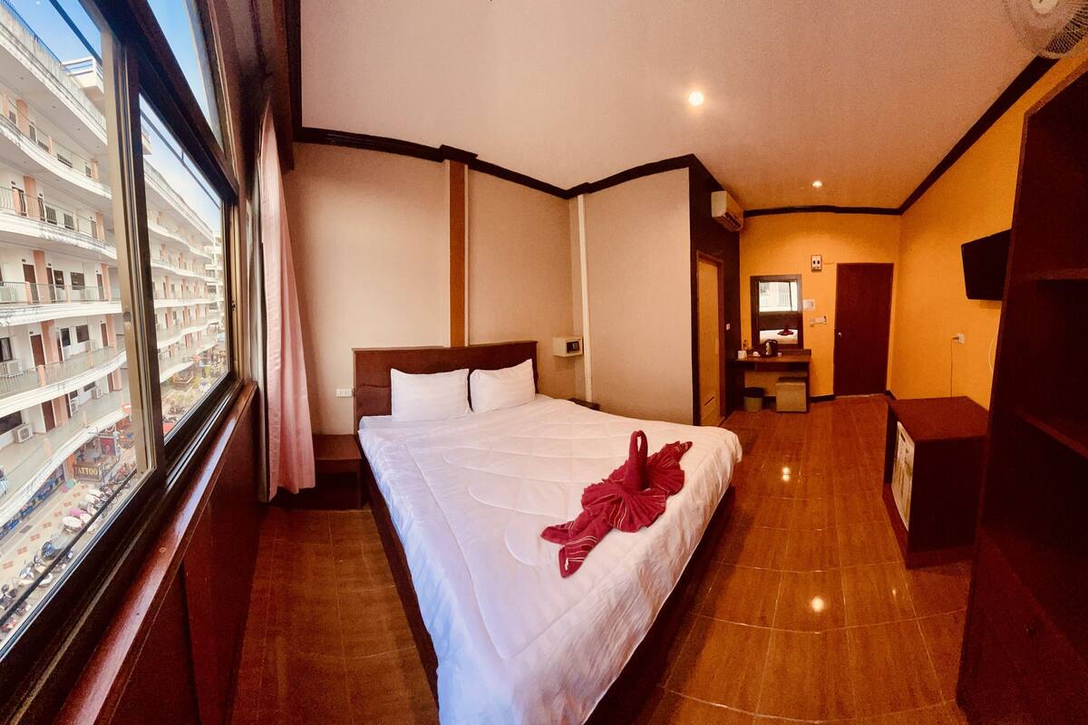 Habitación de hotel con cama, escritorio, televisión y vista a un edificio con balcones.