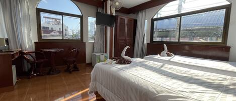 A hotel room with a large bed, a desk, a chair, and a TV.