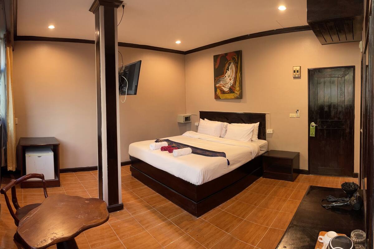 Habitación de hotel con cama, escritorio, silla, televisor y ventana con vista a un edificio.