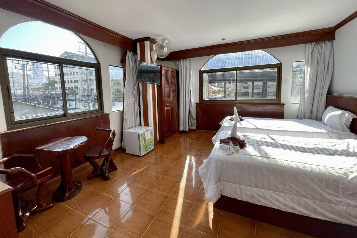 Habitación de hotel con cama, escritorio, silla, televisor y ventanas amplias.