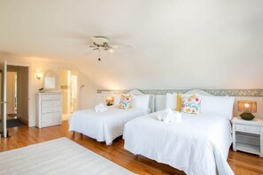 Habitació d'hotel amb dos llits, un ventilador de sostre, una tauleta de nit amb una làmpada i un calaixer blanc.