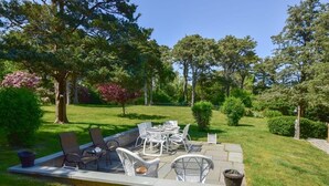 Eine Terrasse im Freien mit Tisch und Stühlen, umgeben von einem gepflegten Rasen und Bäumen.