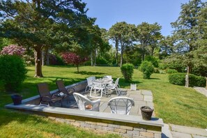 An outdoor patio with a table and chairs, surrounded by a well-maintained lawn and trees.