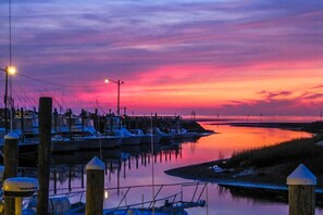 Een jachthaven bij zonsondergang met aangemeerde boten, een steiger en kalm water dat de lucht weerspiegelt.