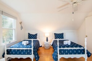 A bedroom with two beds, a ceiling fan, a window, and a nightstand with a lamp.