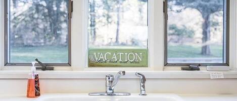 Une salle de bain avec un lavabo, deux robinets et une fenêtre sur laquelle est affiché un panneau indiquant « EN VACANCES ».