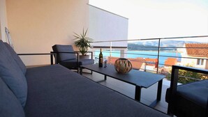 Un balcone con divano, sedie, un tavolo, una pianta in vaso e vista sul mare e sugli edifici.