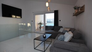 Un soggiorno moderno con un divano grigio, un tavolino da caffè nero e una grande finestra con vista sul mare.