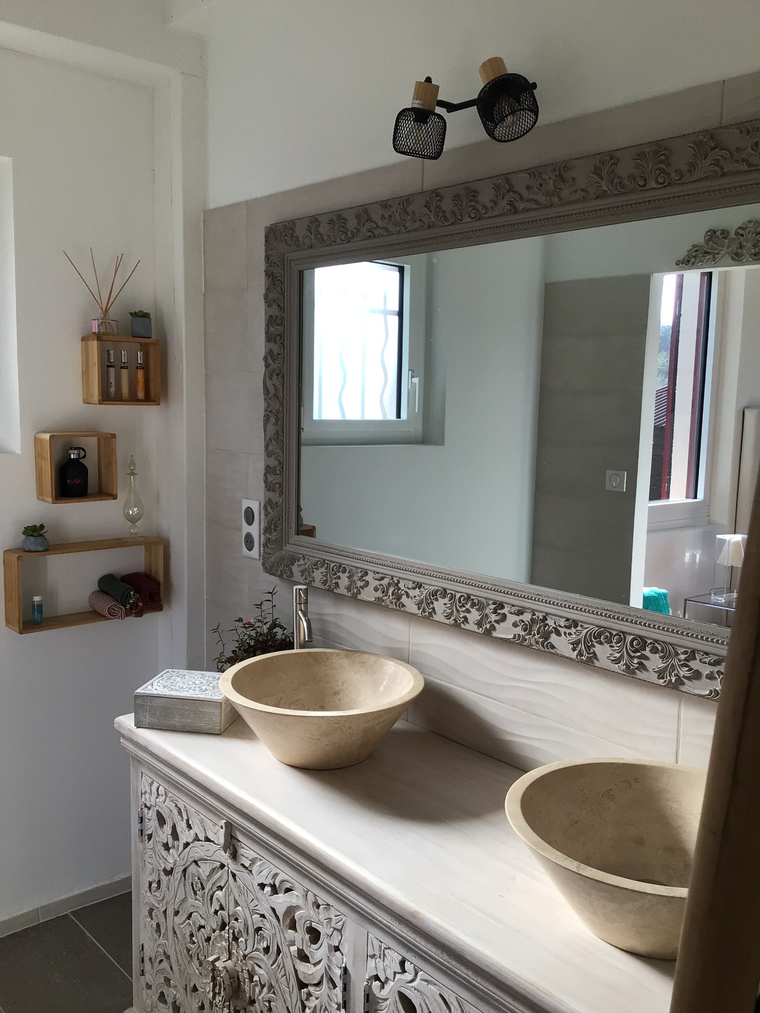 Um banheiro com um espelho grande, duas pias e prateleiras decorativas.