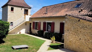 Un bâtiment en pierre de deux étages, avec un toit recouvert de tuiles rouges, un petit balcon et une allée de gravier menant à une terrasse en bois.
