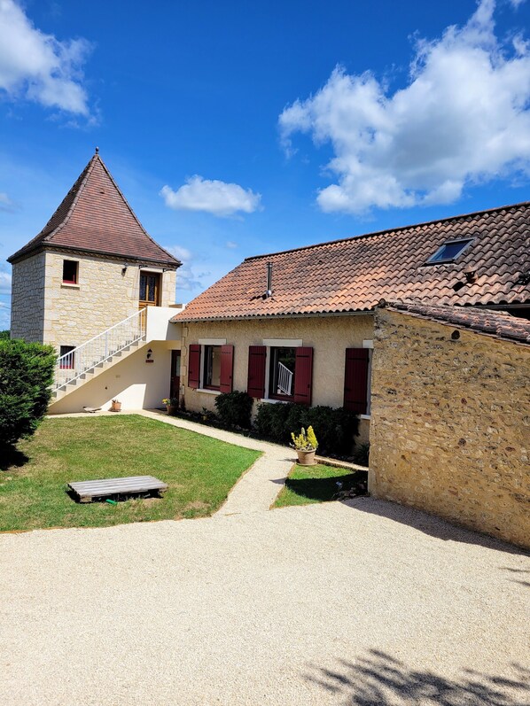 A two-story stone building with a red-tiled roof, a small balcony, and a gravel driveway leading to a wooden deck. - The former barn, house with swimming pool on 5500 m2 of parkland, (Le Buisson-de-Cadouin)