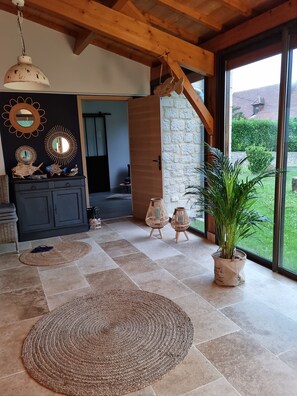 A spacious living area with a stone wall, wooden ceiling beams, and a large window offering a view of the outdoors. - The former barn, house with swimming pool on 5500 m2 of parkland, (Le Buisson-de-Cadouin)