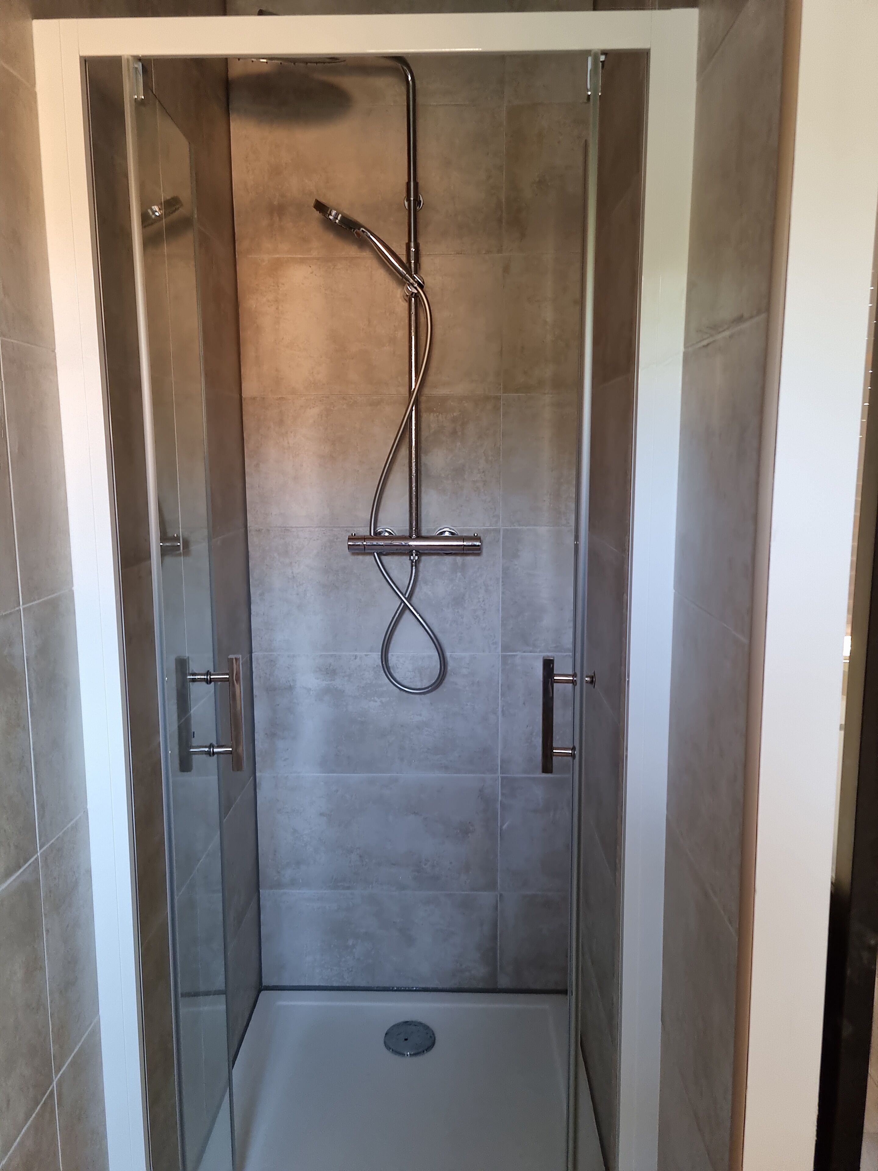 Douchecabine met een glazen deur, een handdouche en een wandmengkraan.