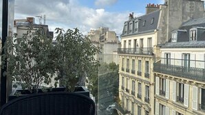 A balcony with a table set for two, overlooking a cityscape with historic buildings. - CARD Hôtel (Paris)