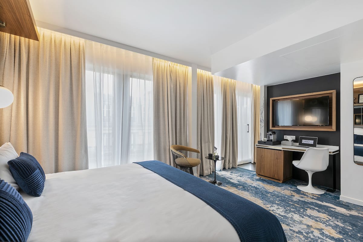 A hotel room with a large bed, a desk with a computer, a chair, and a TV.