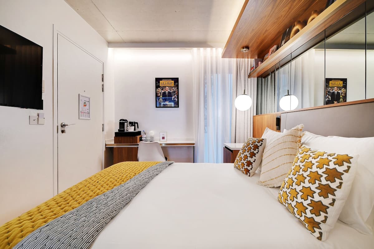 A hotel room with a large bed, a desk, and a mirror.