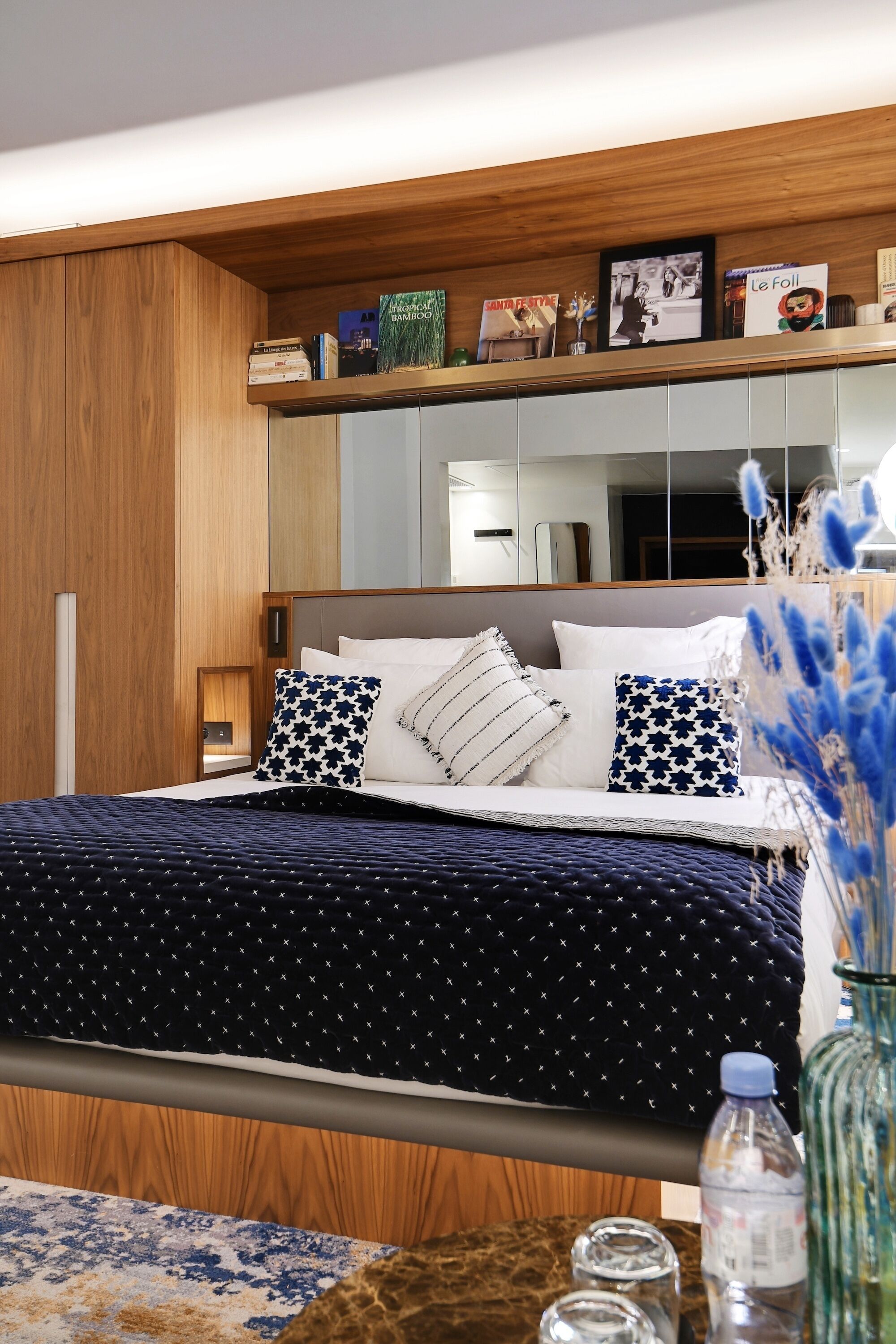 A bedroom with a bed, pillows, a bedside table with a water bottle, and a mirror.