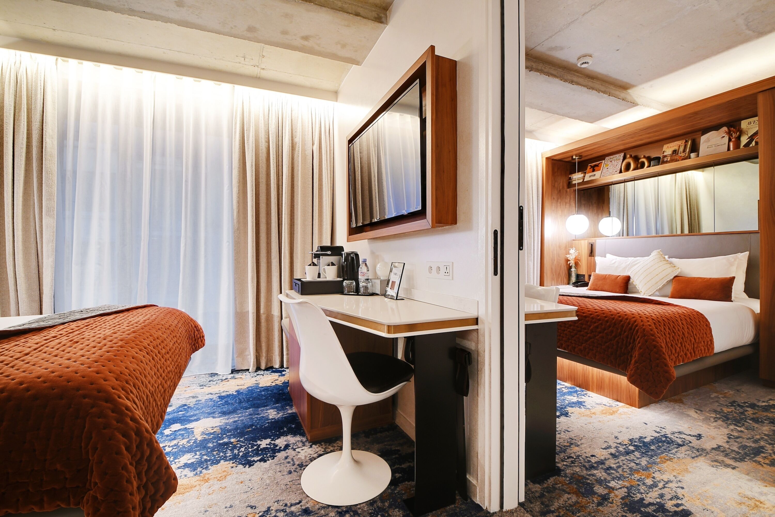 A hotel room with two beds, a desk, a chair, a mirror, and a small table with a coffee maker.