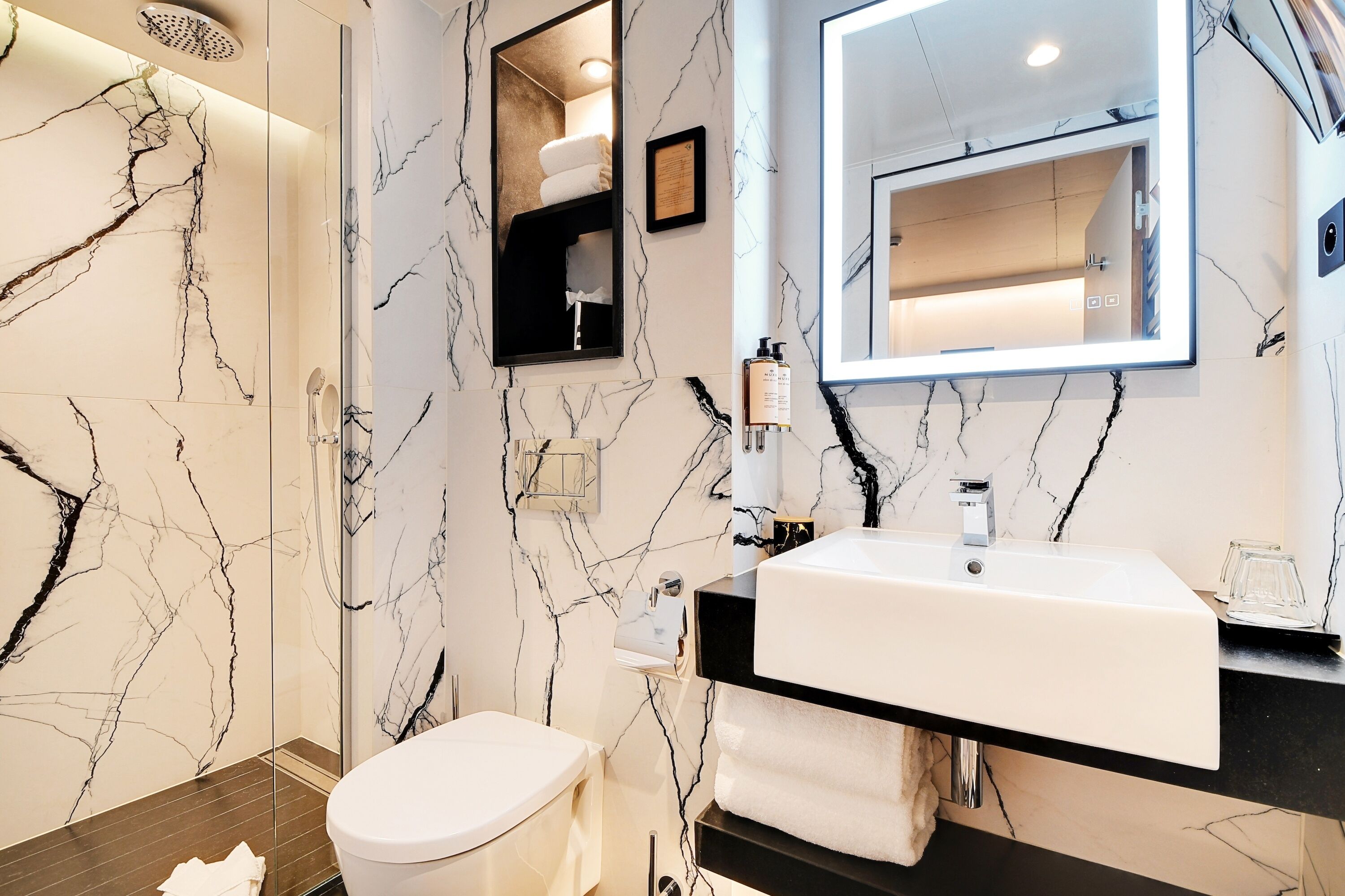 Un baño moderno con un lavamanos blanco, encimera negra y paredes con diseño de mármol.